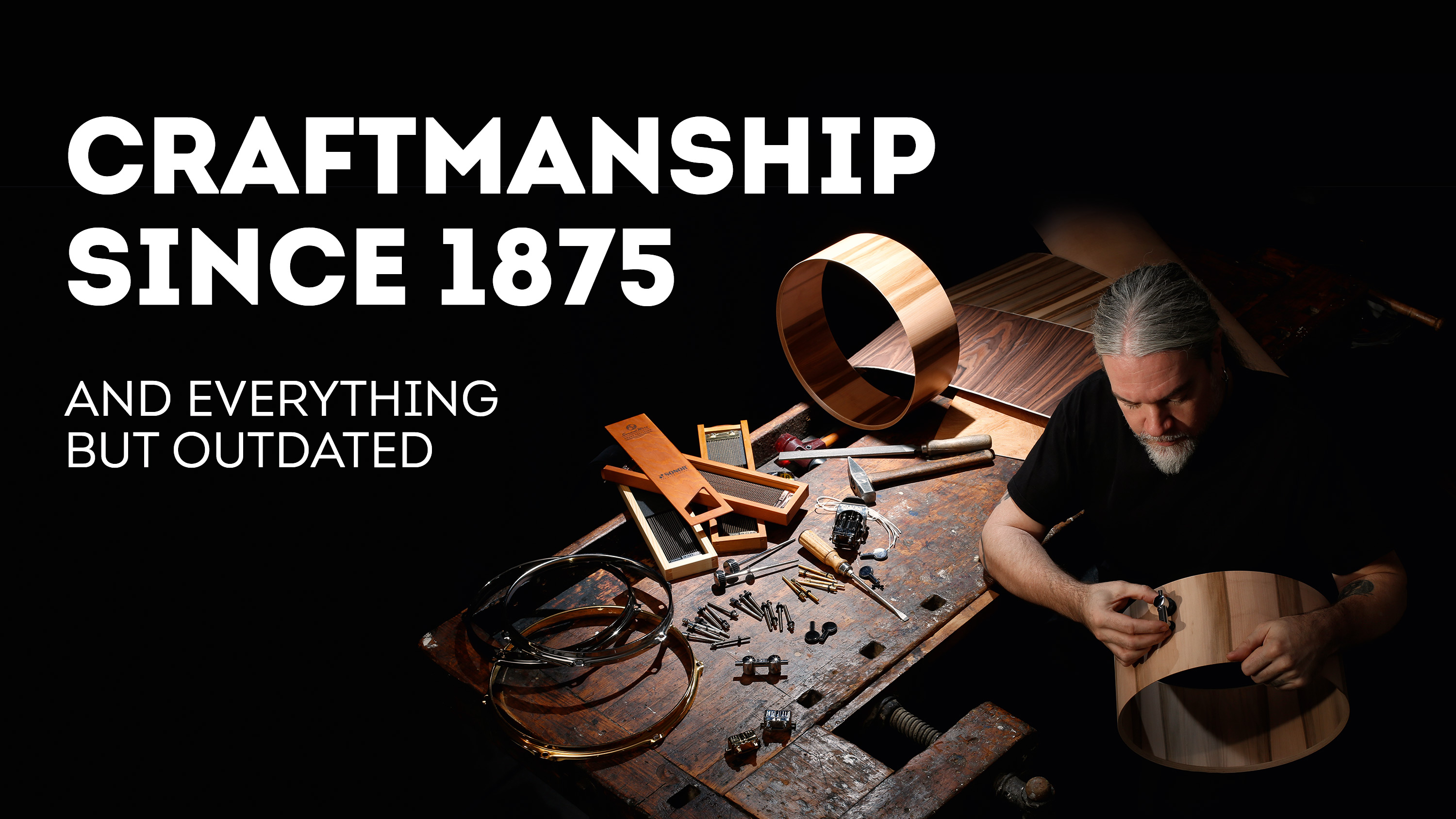 An older man standing at a dramatically lit workbench is holding a fastener against a wooden drum, accompanied by the promotional headline "Craftsmanship since 1875"